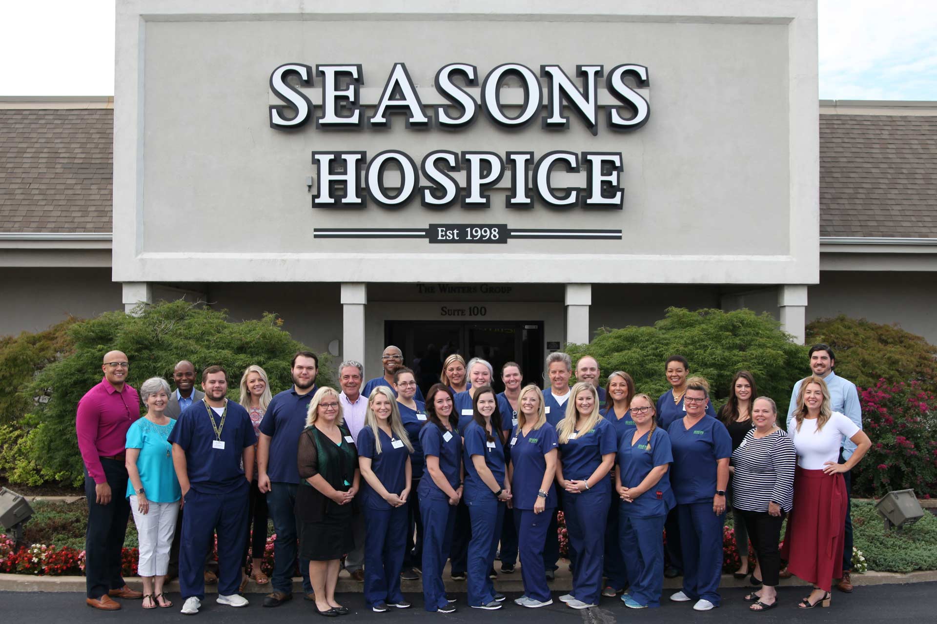 Seasons Hospice staff gather outside the front doors of the facility to pose for a group photo.